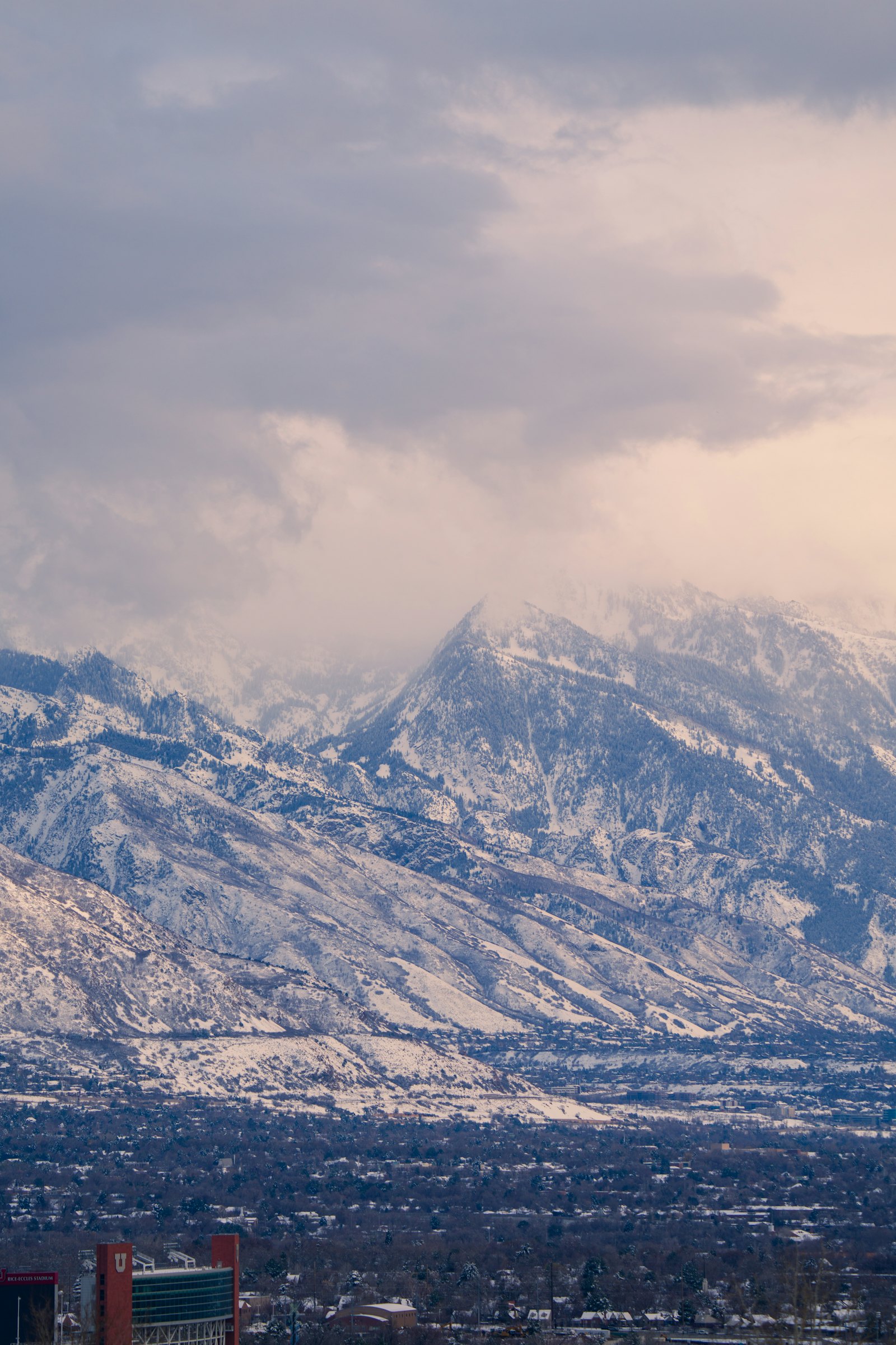 Snowy Wasatch peaks towering over Salt Lake City under a cloudy sky.